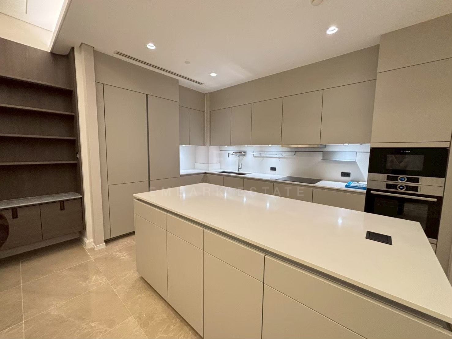 The kitchen at Sindhorn Kempinski, a long island in white stone with pale full-height cabinetry and integrated ovens