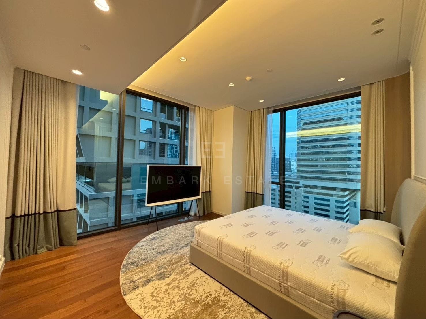 A bedroom of the 157 square metre residence at Sindhorn Kempinski, timber floors and a round rug with glazing on two sides over the central Bangkok skyline