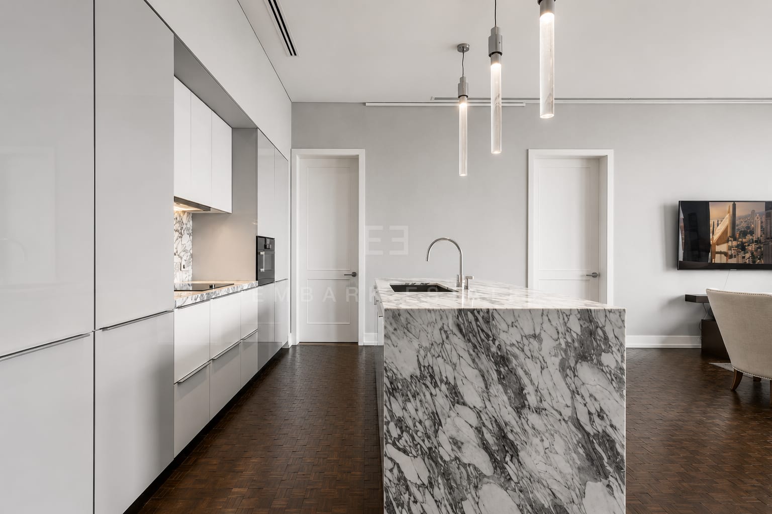 The kitchen of the 133 square metre residence at The Ritz-Carlton Residences Bangkok, an Arabescato marble island under tube pendants with white gloss cabinetry along the wall