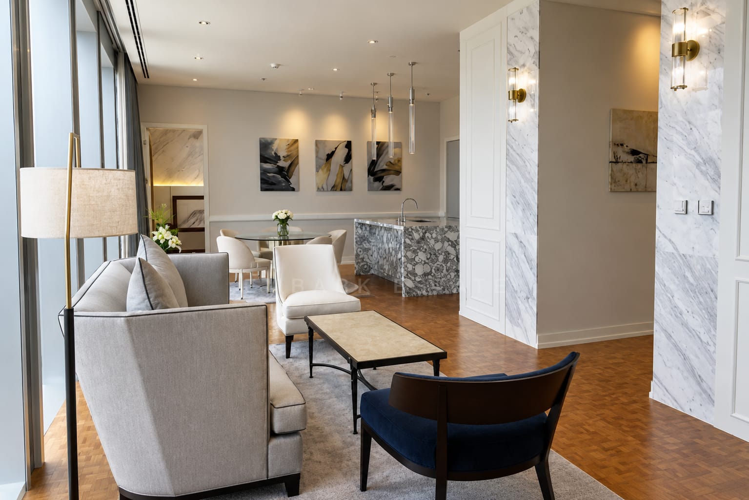 The living room of the 145 square metre residence at The Ritz-Carlton Residences Bangkok, seating on a rug between marble-clad columns with the dining table and kitchen island beyond