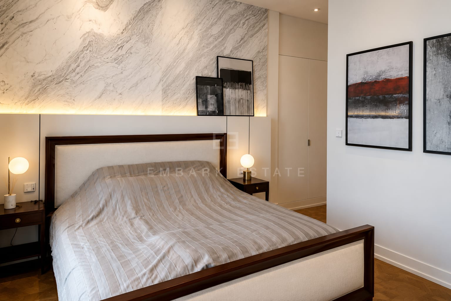 A bedroom at The Ritz-Carlton Residences Bangkok, a marble feature wall behind the bed with a backlit ledge and lamps to either side