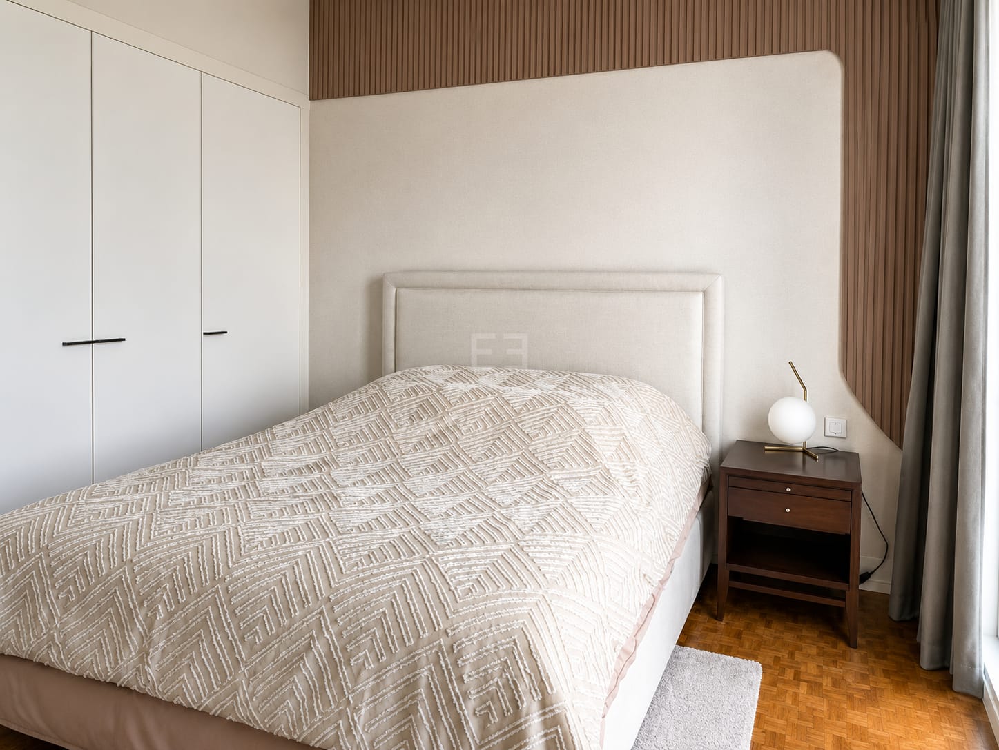 A bedroom at The Ritz-Carlton Residences Bangkok, an upholstered headboard against fluted timber panelling with fitted wardrobes alongside