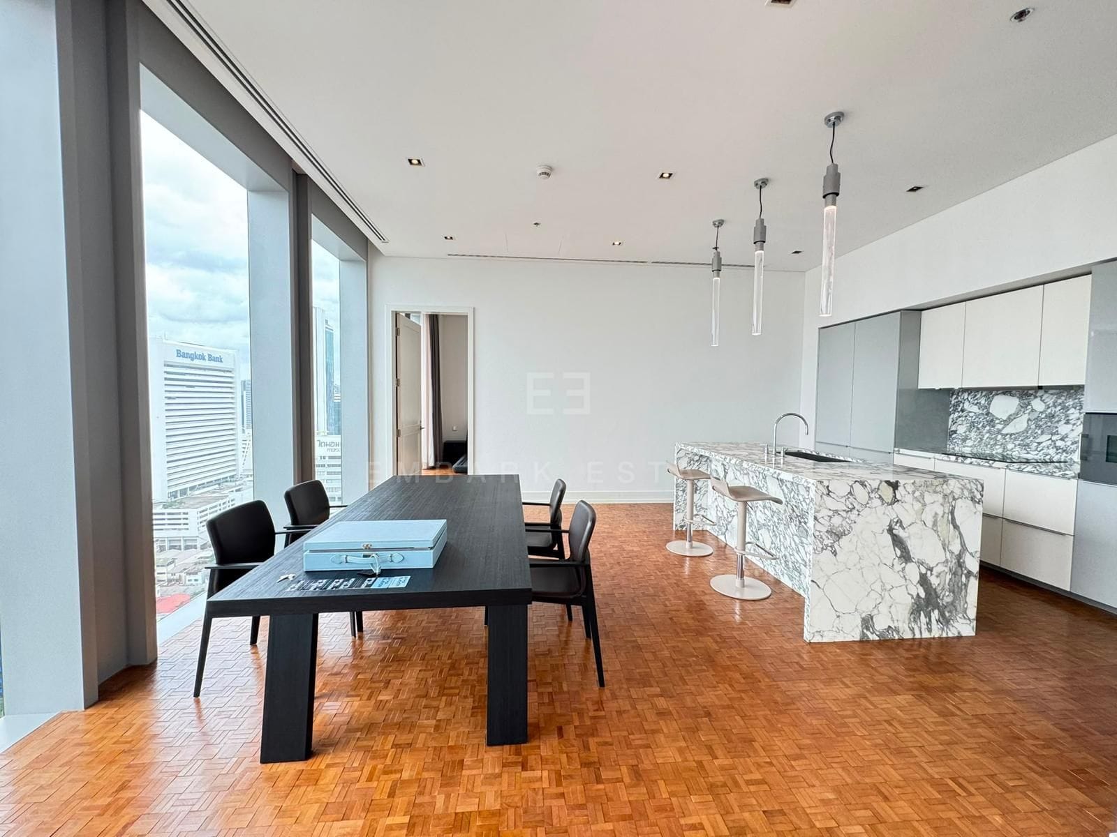 The dining area and open kitchen at The Ritz-Carlton Residences Bangkok on the 25th floor, a veined marble island beside the dining table and full-height glazing