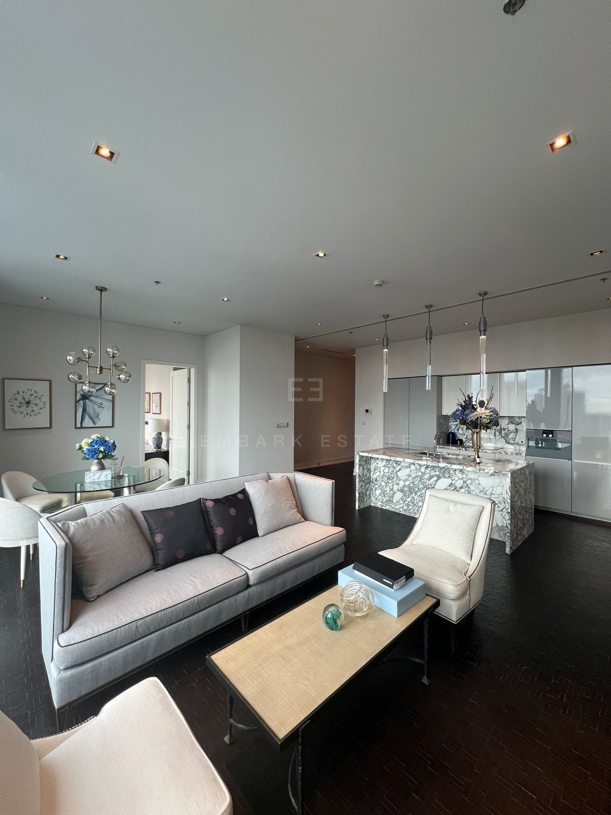The living and dining room at The Ritz-Carlton Residences Bangkok, pale seating on dark timber floors beneath a run of pendants
