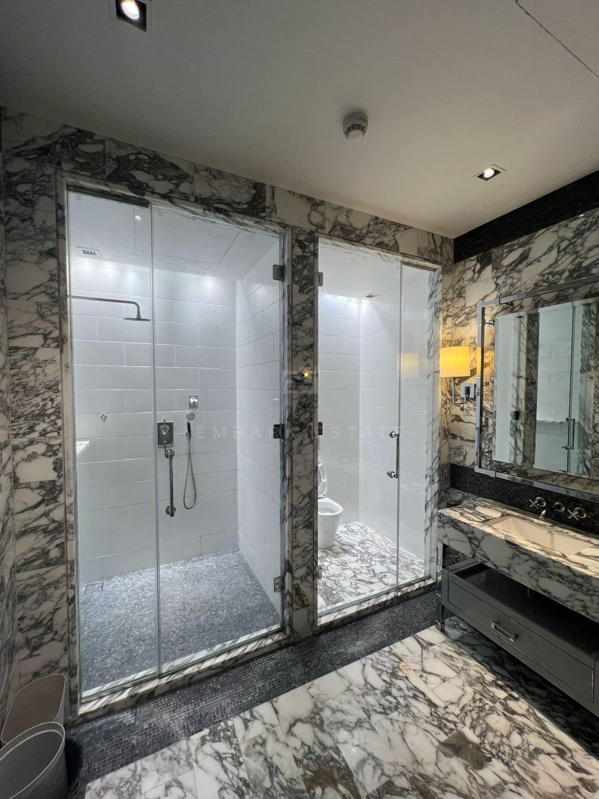 The shower room at The Ritz-Carlton Residences Bangkok, glass against veined marble with a marble vanity alongside