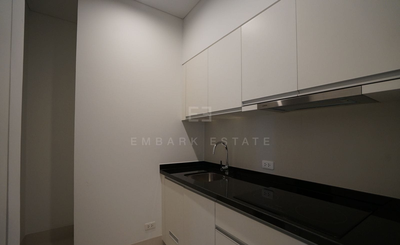 The galley kitchen of the 199 sq.m residence at The Ritz-Carlton Residences Bangkok, white cabinetry with a black stone counter and induction hob