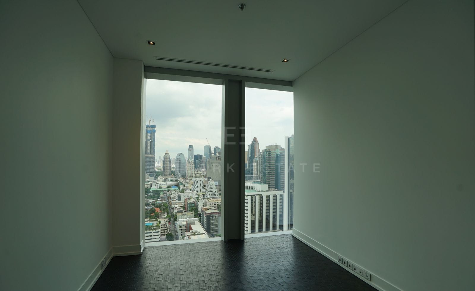 An empty bedroom at The Ritz-Carlton Residences Bangkok, dark timber floor and full-height glazing over the skyline