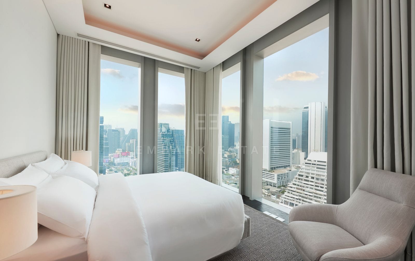 The master bedroom of the 210 sq.m residence at The Ritz-Carlton Residences Bangkok, corner floor-to-ceiling glazing over the city and an upholstered reading chair