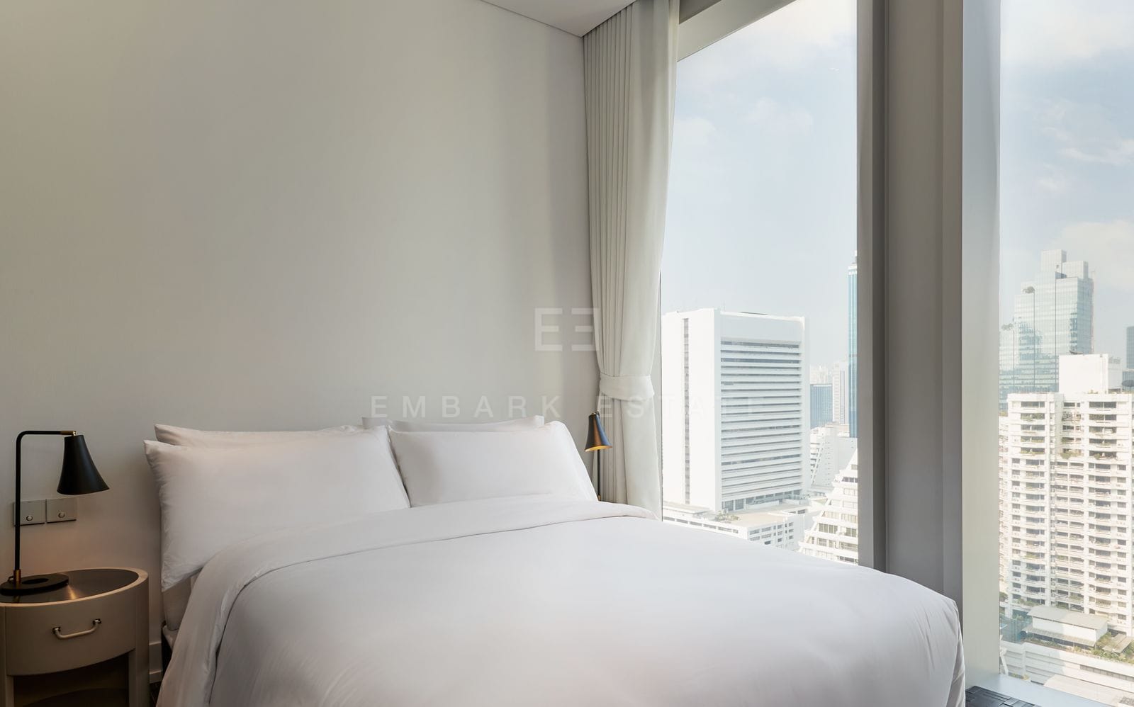 A bedroom at The Ritz-Carlton Residences Bangkok, the bed facing full-height windows over the Sathorn towers