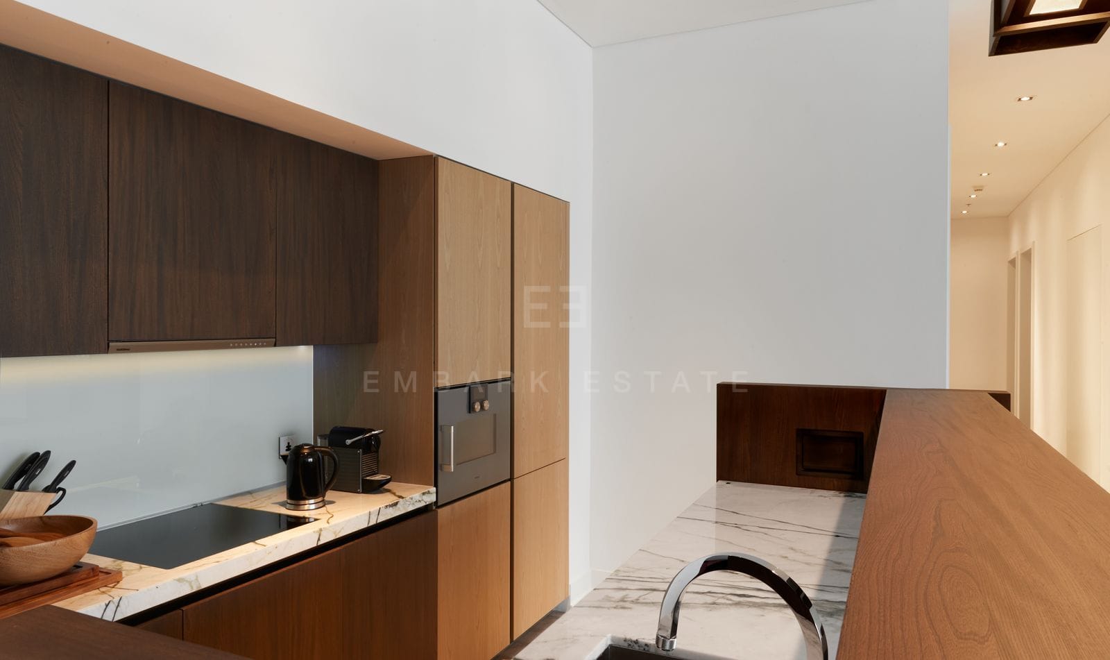 The kitchen counter of the residence, dark timber cabinetry under a marble worktop with integrated appliances