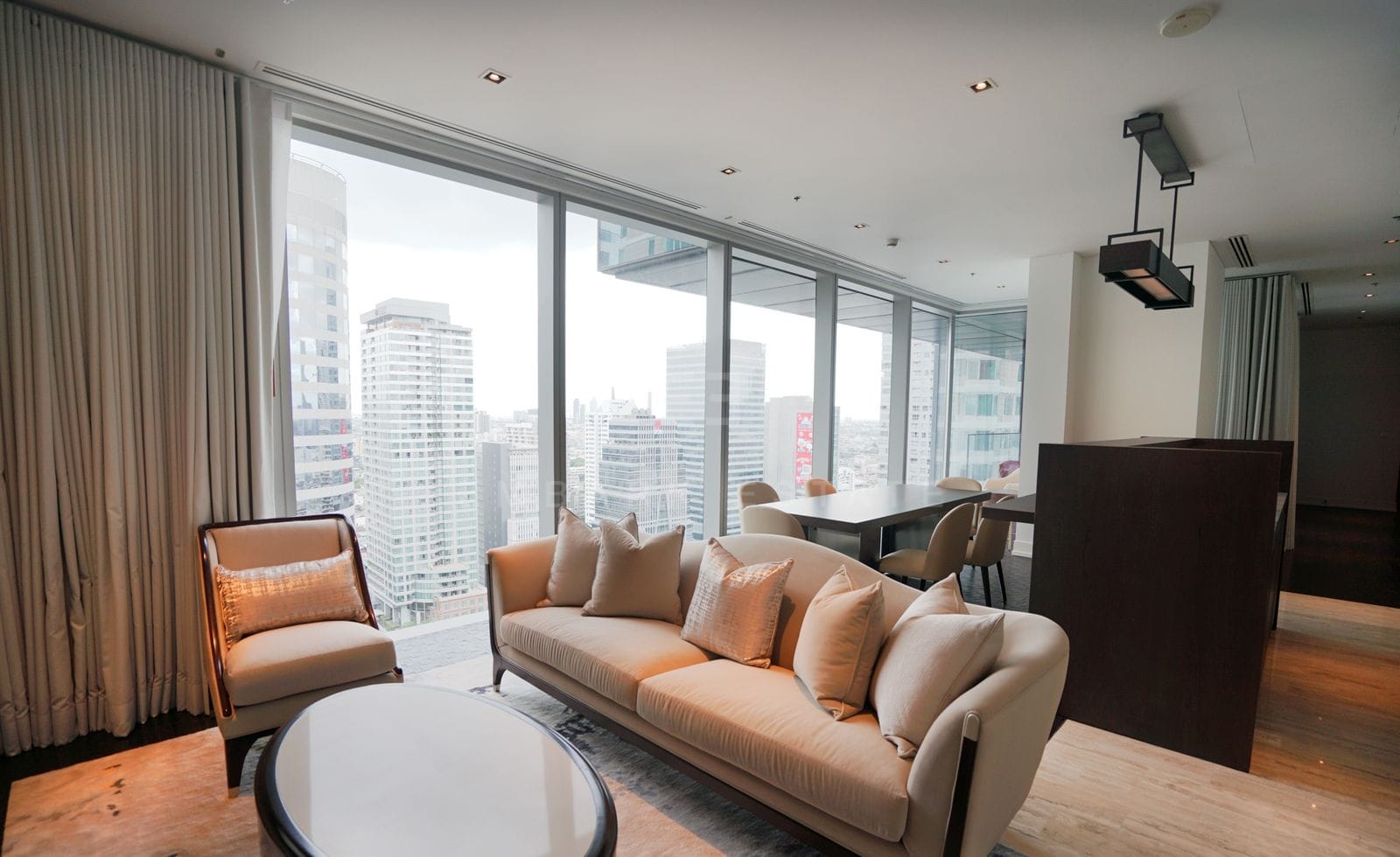 The living room of the 211 sq.m residence at The Ritz-Carlton Residences Bangkok, a taupe sofa and armchair by the curtained corner glazing
