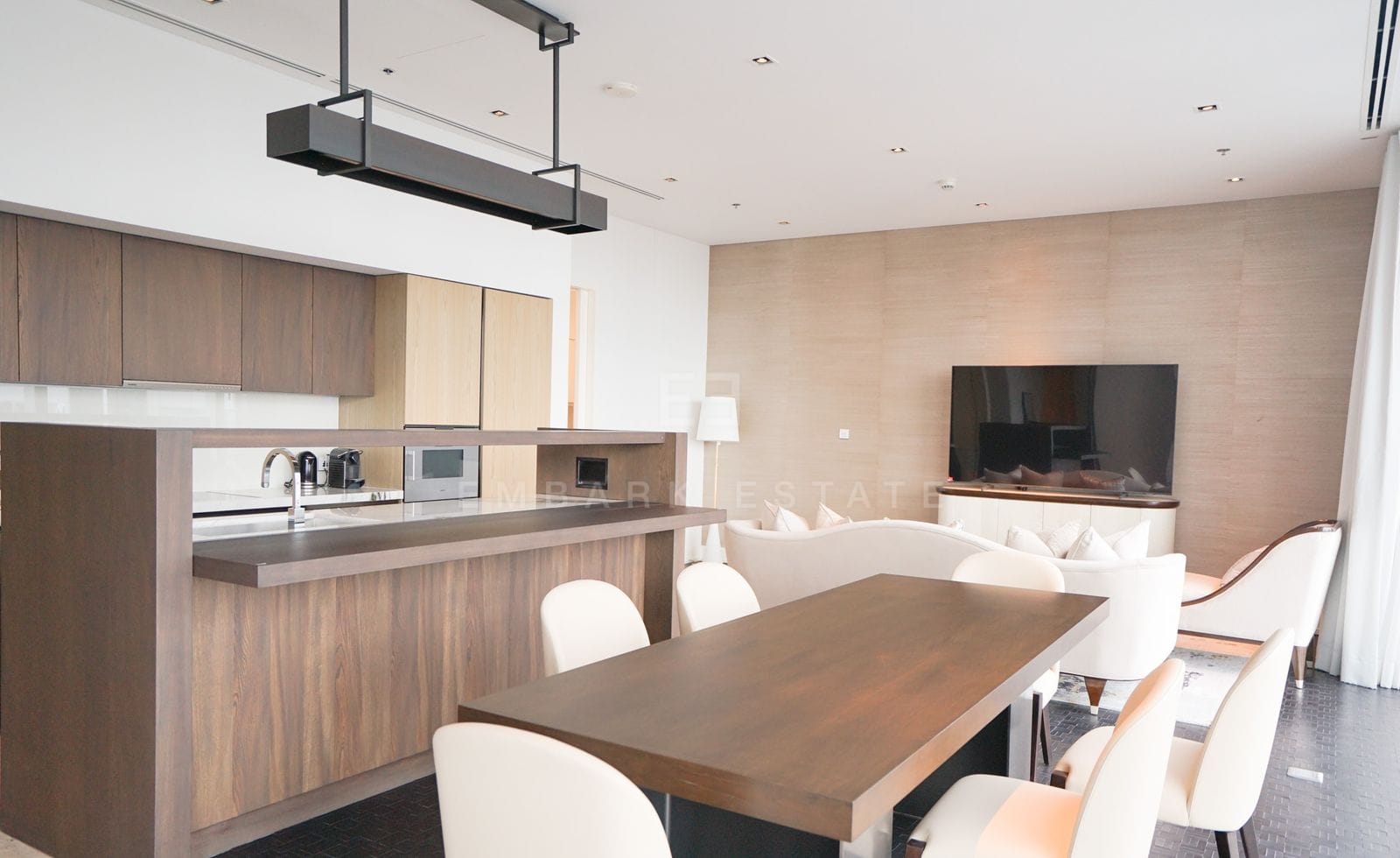 The dining table and white chairs beside the kitchen at The Ritz-Carlton Residences Bangkok, the television lounge beyond