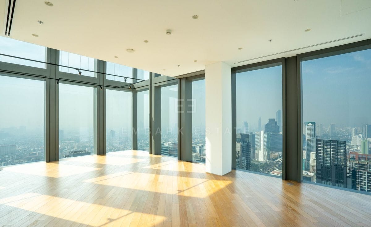 The double-height living room at The Ritz-Carlton Residences Bangkok, glazing on two sides and sunlight across the oak floor
