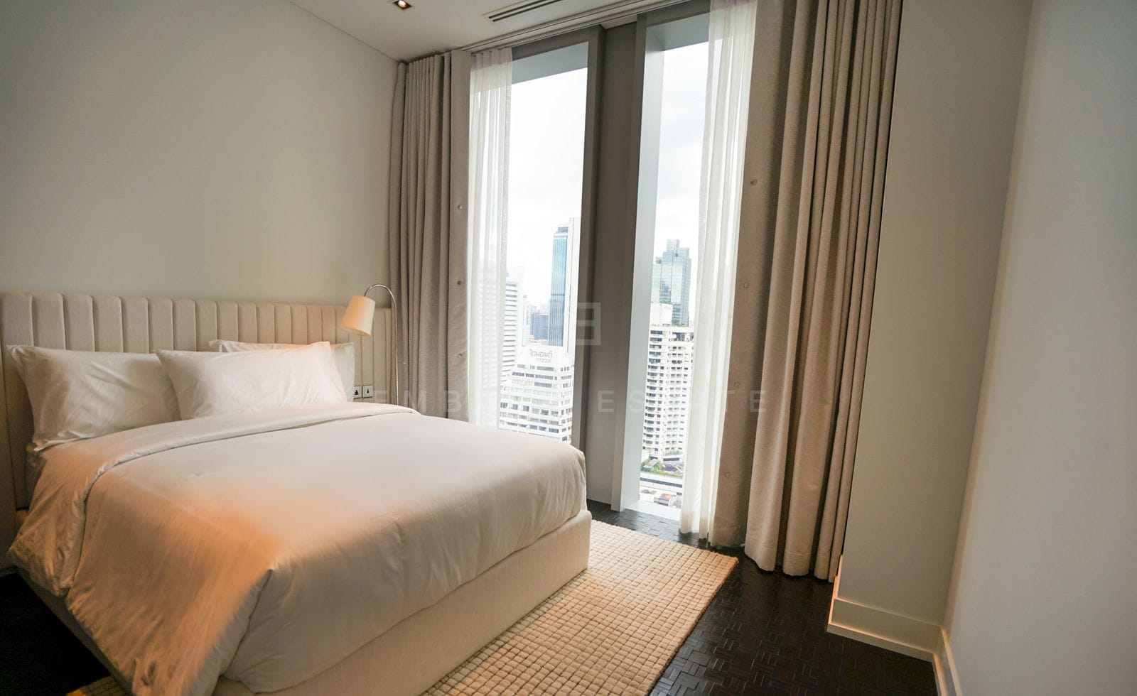 A furnished bedroom at The Ritz-Carlton Residences Bangkok, a channel-stitched headboard and full-height windows over the city