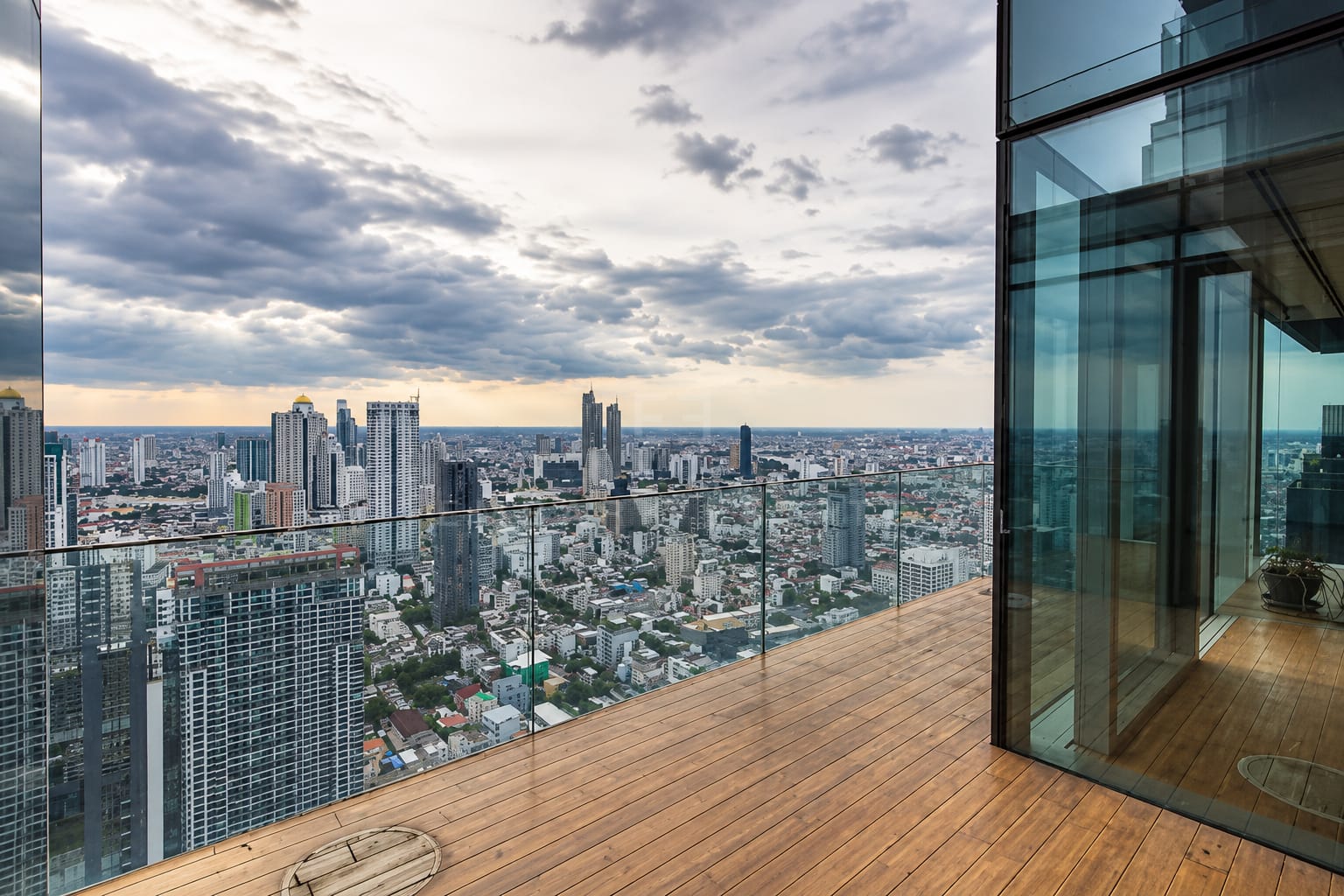 The terrace at The Ritz-Carlton Residences Bangkok at dusk, timber decking behind a glass balustrade above the city