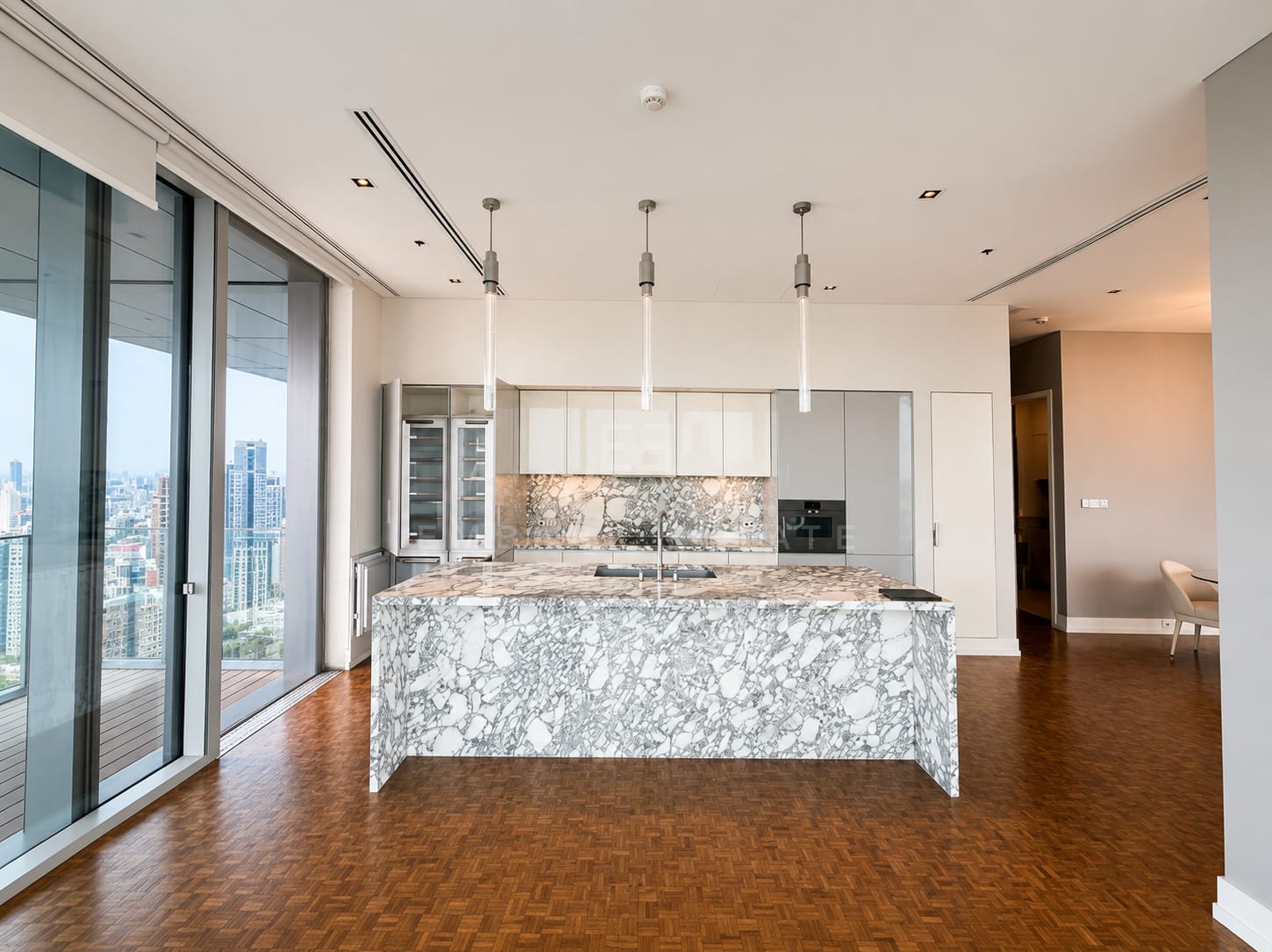 The kitchen island at The Ritz-Carlton Residences Bangkok in Arabescato marble, glass-fronted wine storage behind and sliding glass onto the terrace