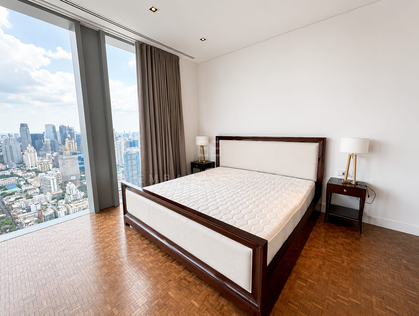 A bedroom of the 248 square metre residence at The Ritz-Carlton Residences Bangkok, a dark timber bed frame between brass lamps with full-height glazing over the city