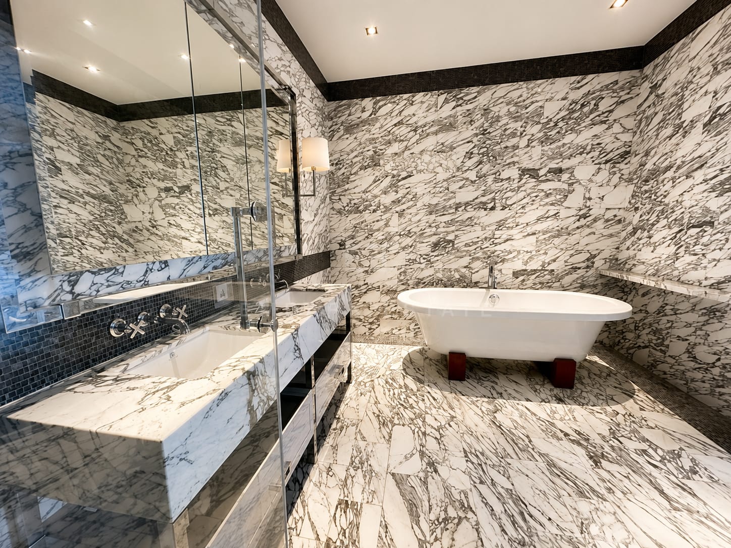 The main bathroom at The Ritz-Carlton Residences Bangkok, a roll-top tub on floor and walls of Arabescato marble with a dark mosaic border