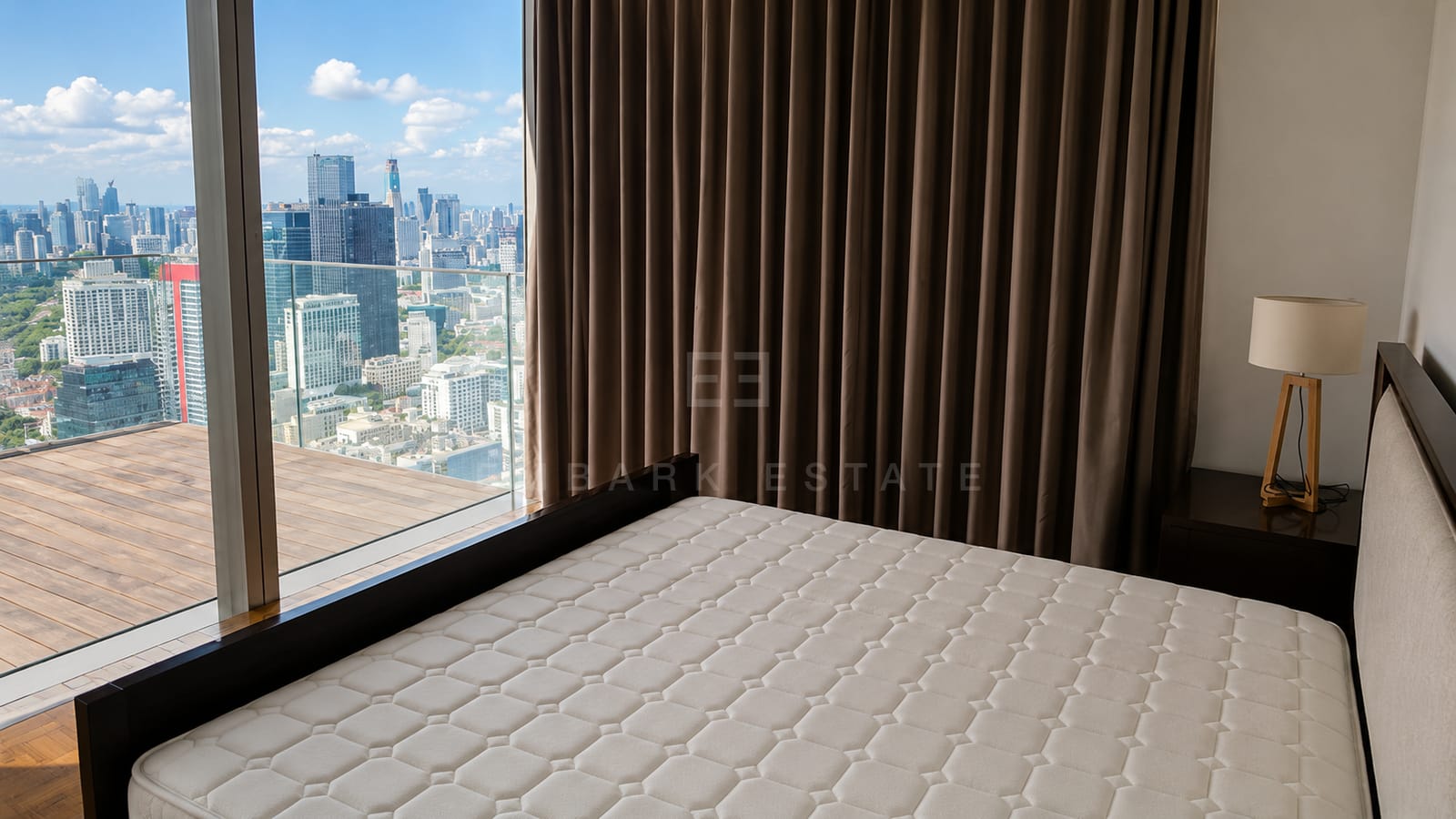 A bedroom at The Ritz-Carlton Residences Bangkok, a dark timber bed base and a brass lamp beside glazing onto the terrace