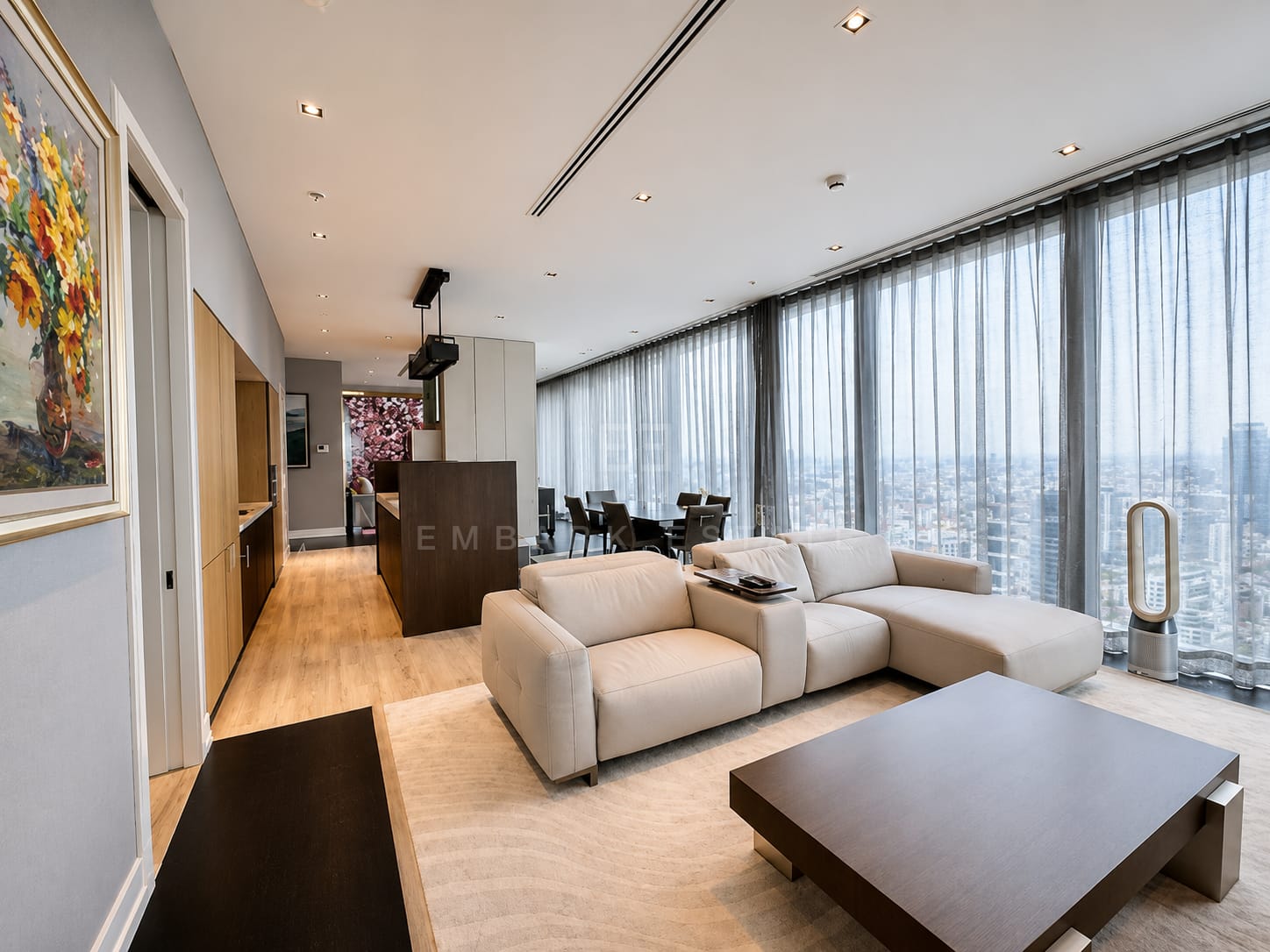 The living room of the 273 square metre residence at The Ritz-Carlton Residences Bangkok, a cream sectional on a pale rug with sheer curtains along the full-height glazing