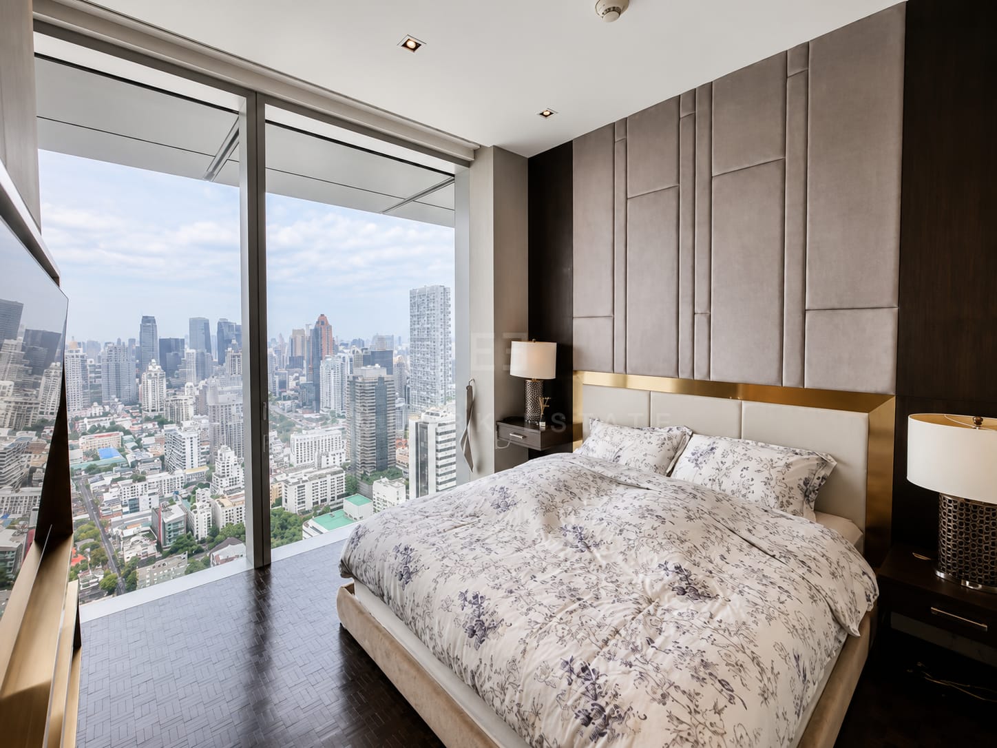 A bedroom at The Ritz-Carlton Residences Bangkok, an upholstered panelled headboard wall with a brass band and sliding glass onto the balcony
