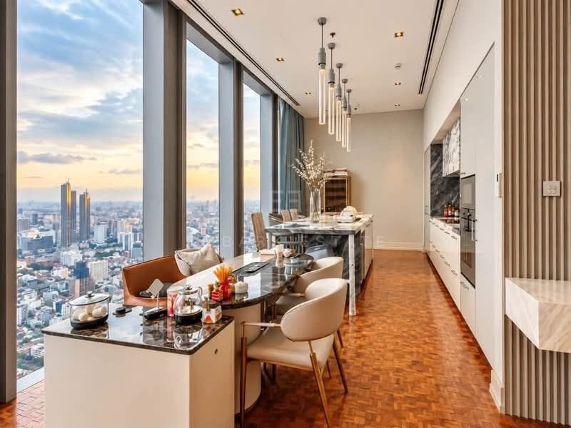 The dining table at The Ritz-Carlton Residences Bangkok beneath glass pendant lights, set against full-height windows over the Sathorn skyline at dusk