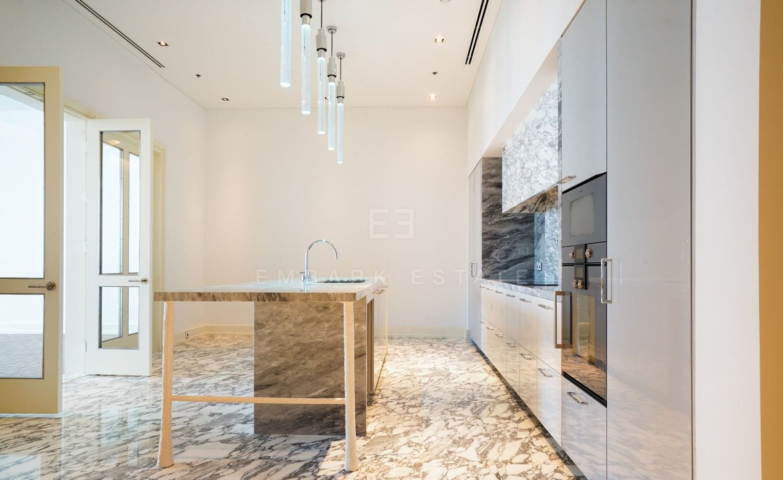 The kitchen at The Ritz-Carlton Residences Bangkok, an Arabescato marble island under glass pendant lights with ovens and grey lacquered cabinetry