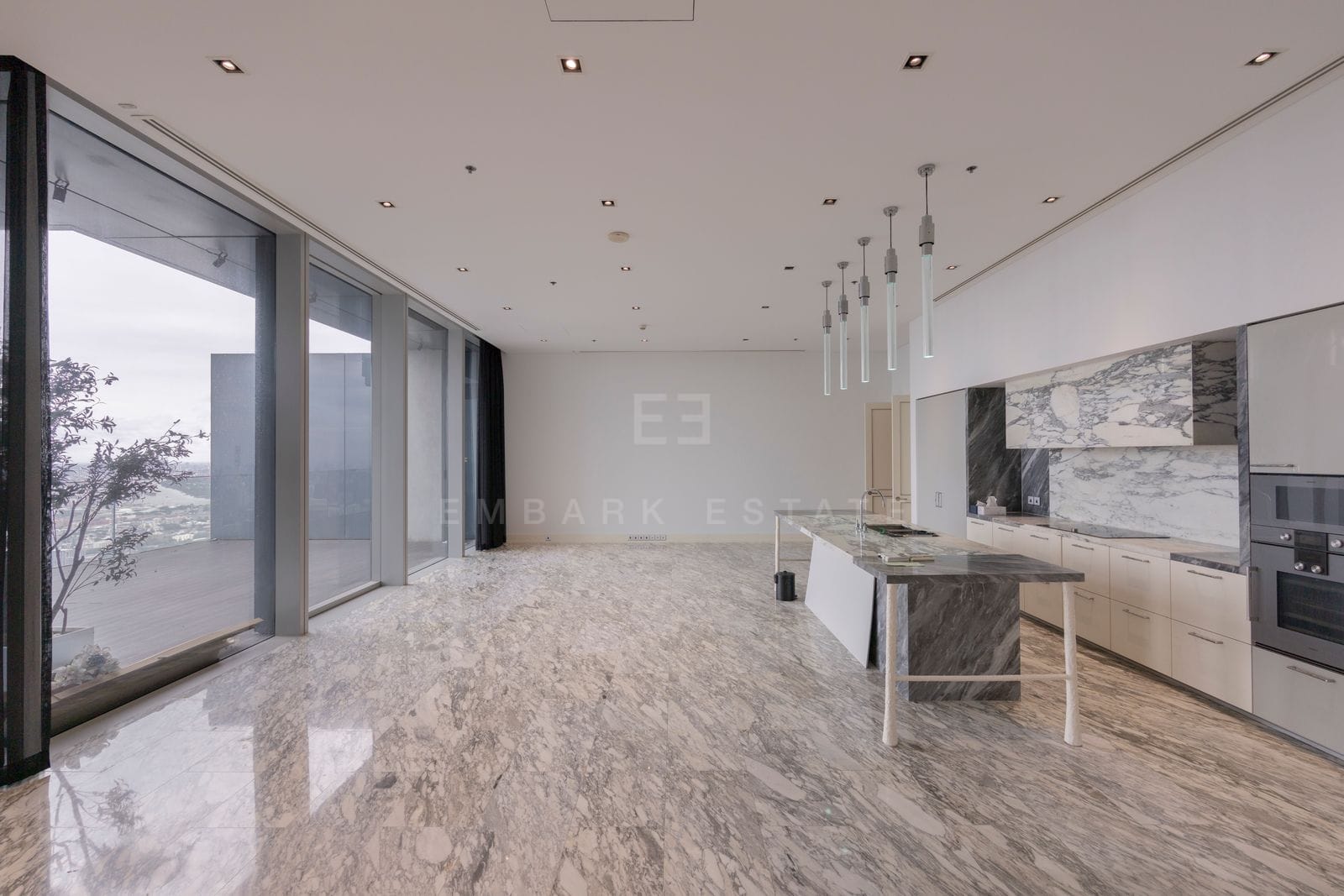 The open kitchen and living room of the Sky Residence at The Ritz-Carlton Residences Bangkok on level 63, a stone island beneath glass pendants with the terrace and the city beyond