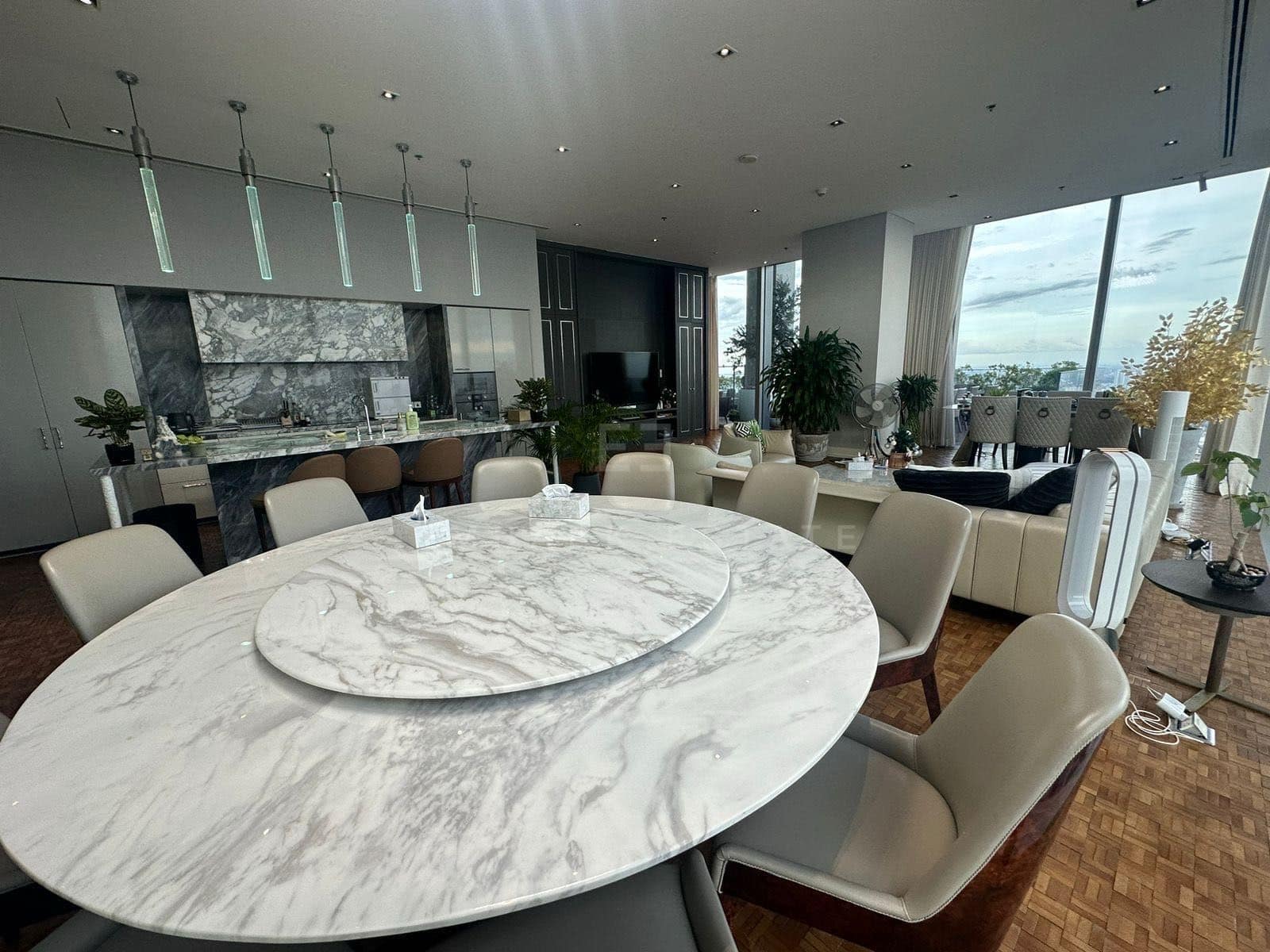 The dining table of the Sky Residence on level 61 at The Ritz-Carlton Residences Bangkok, an oval marble top with a marble lazy Susan and the kitchen behind