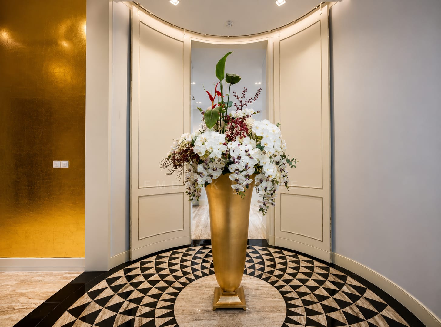 The entrance hall at The Ritz-Carlton Residences Bangkok, curved panelled walls and a gold leaf panel above a geometric mosaic medallion in the floor