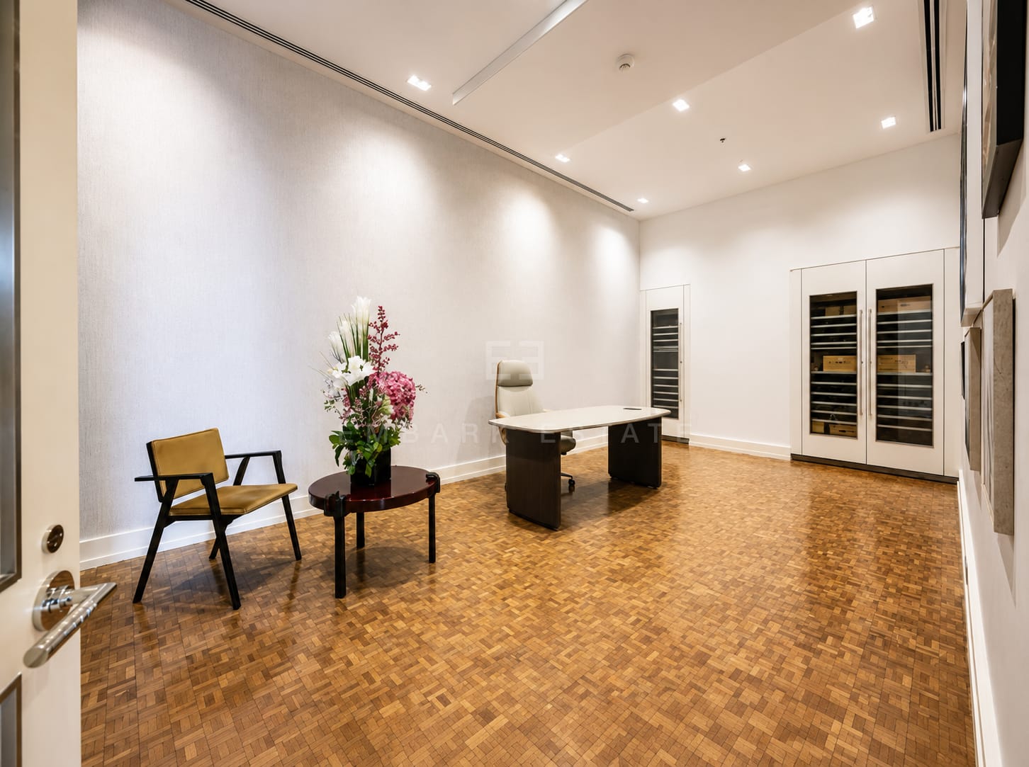 The study at The Ritz-Carlton Residences Bangkok, a desk on parquet with glazed wine cabinets built into the wall opposite