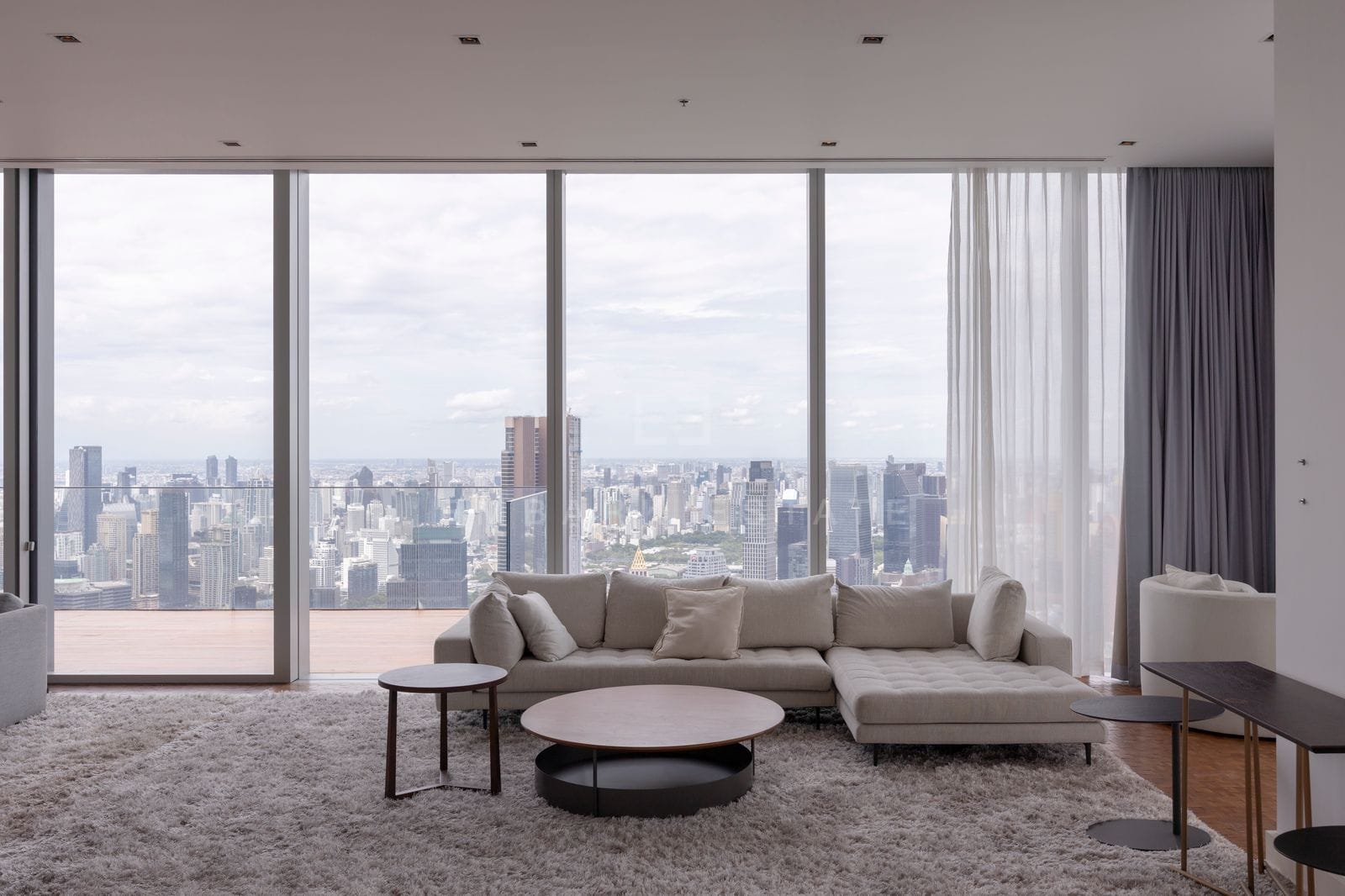 Living room at The Ritz-Carlton Residences Bangkok, floor 69, a long sofa on a pale rug beneath full-height glazing over the city