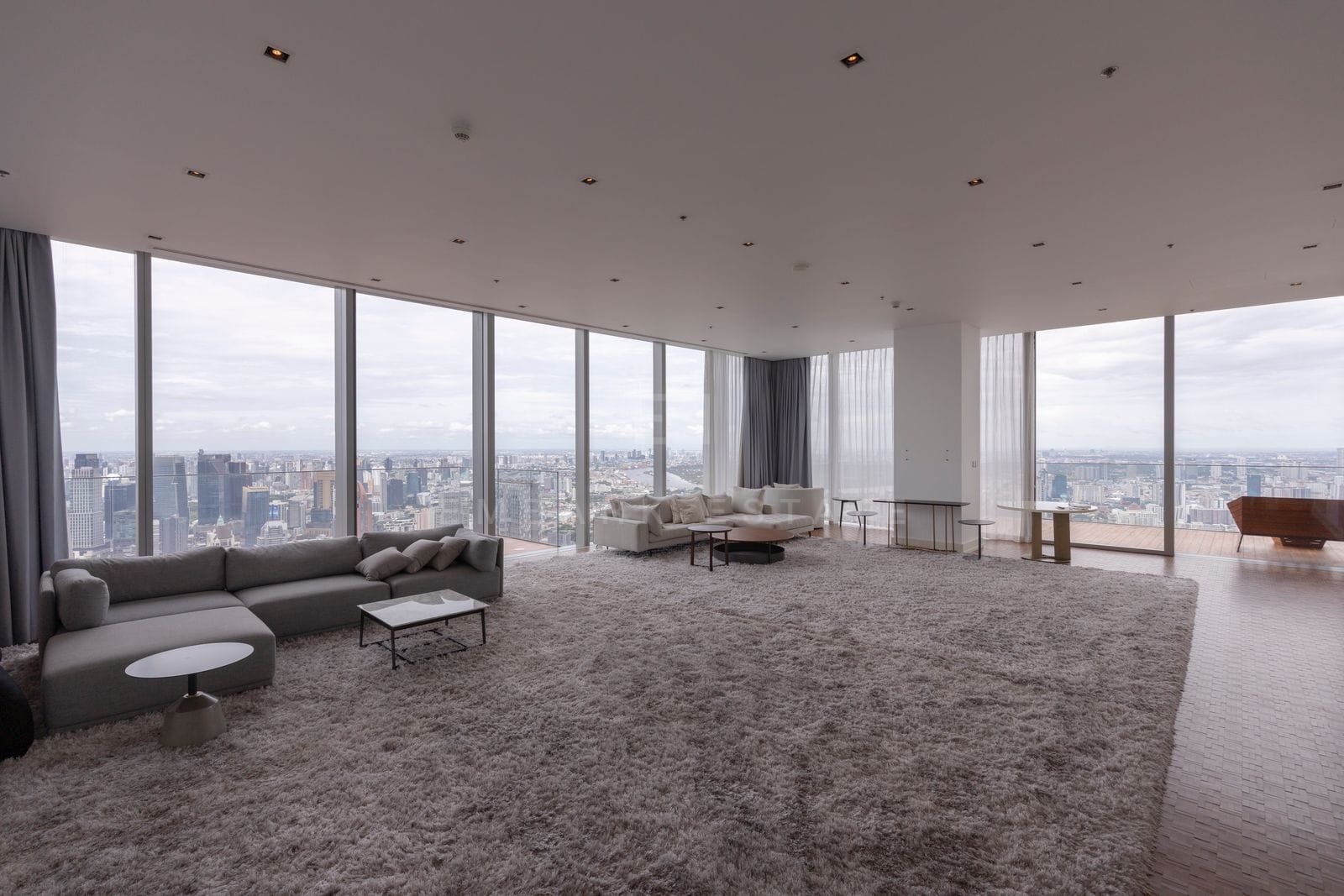 The living room at The Ritz-Carlton Residences Bangkok wrapped in floor-to-ceiling glass, with the Bangkok skyline on two sides