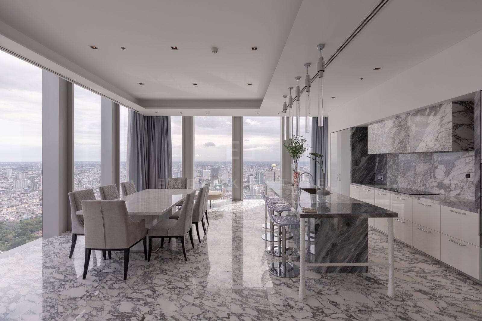 The marble kitchen and dining room at The Ritz-Carlton Residences Bangkok, veined stone island and backsplash under glass pendants
