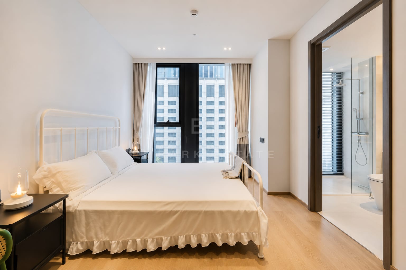 A bedroom at Tonson One Residence, a white metal bed frame with its bathroom and glazed shower through the door