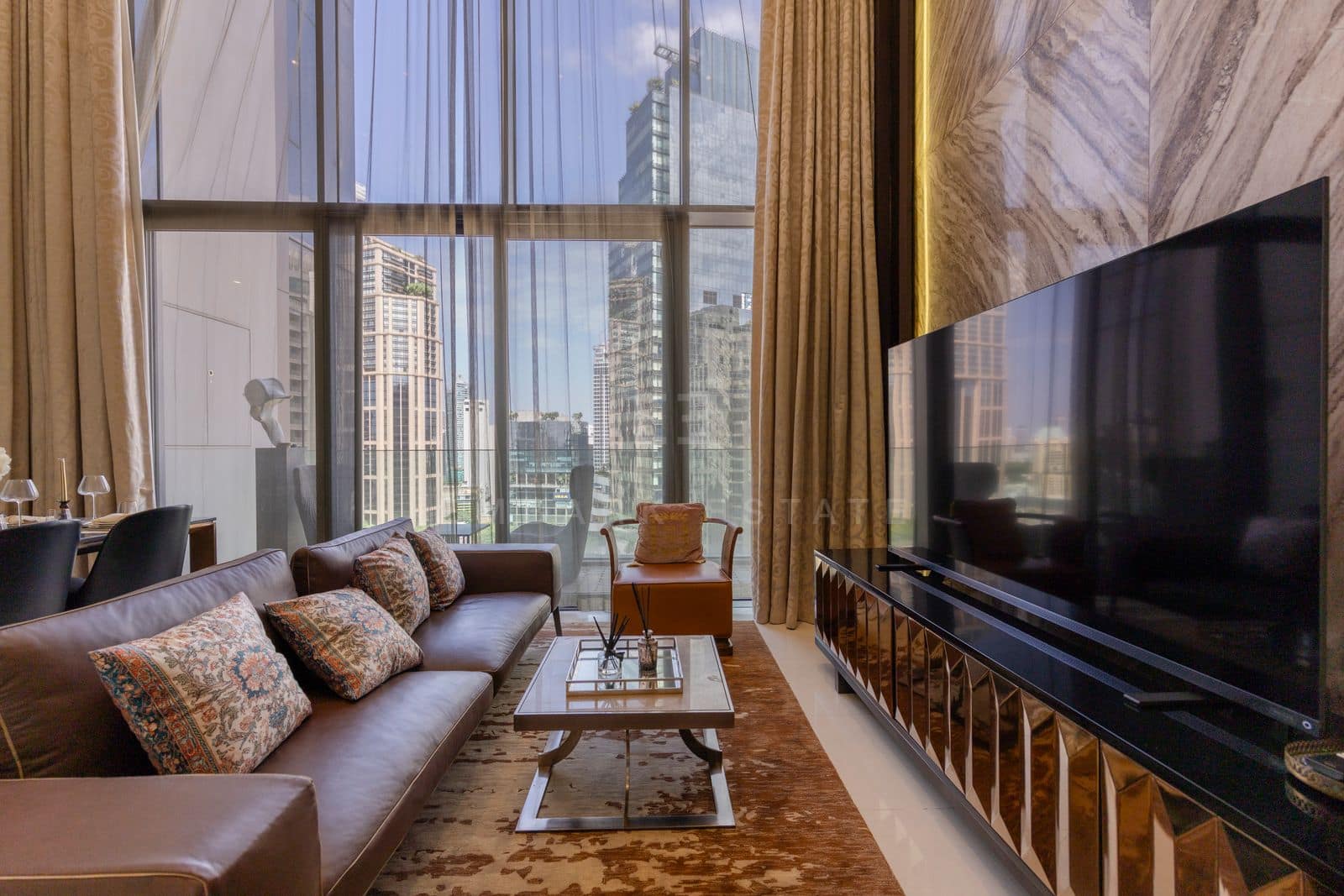 The living room of the 168 square metre duplex at Vittorio Sukhumvit 39, the sofa facing a wall-mounted television with the Sukhumvit skyline through full-height glazing