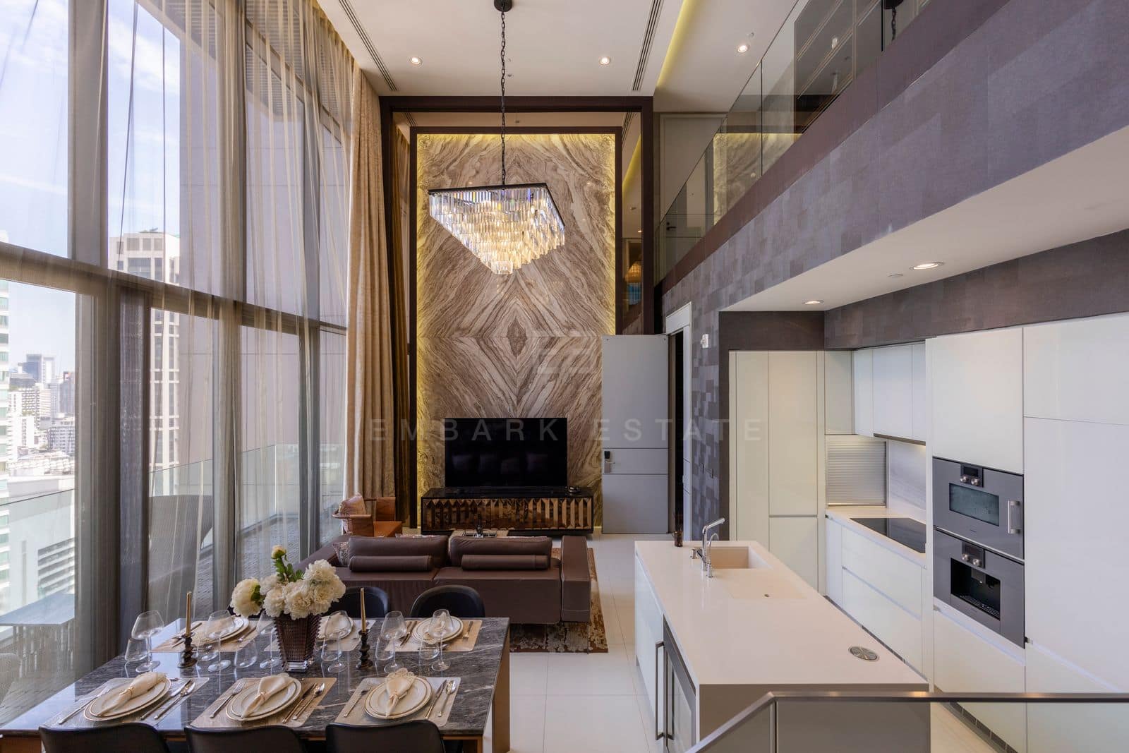 The living and dining room of the 168 square metre duplex at Vittorio Sukhumvit 39, seen from the kitchen, a Palissandro marble feature wall rising the full two storeys