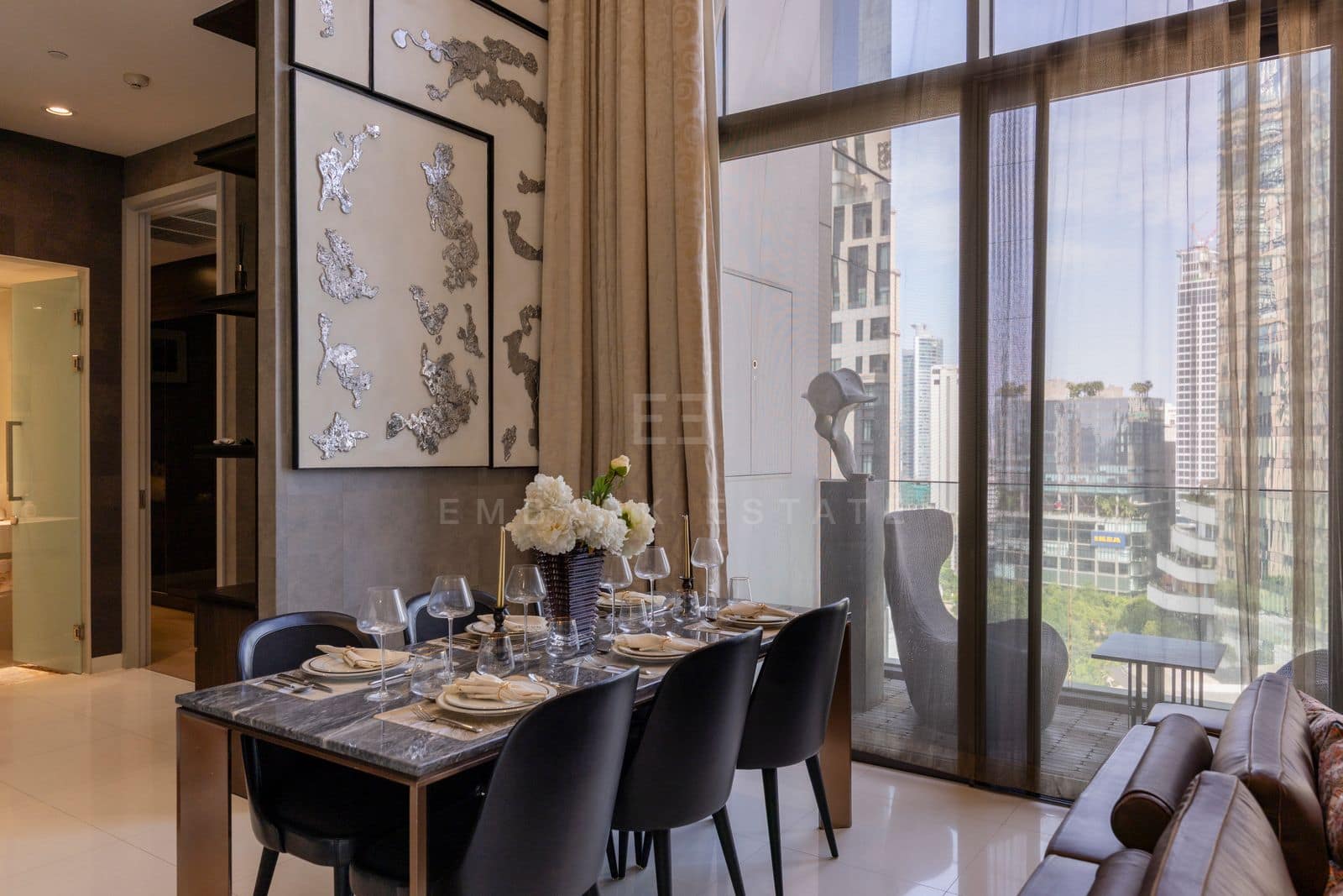 The dining table of the 168 square metre duplex at Vittorio Sukhumvit 39, set for six beside the window wall, with the living room beyond