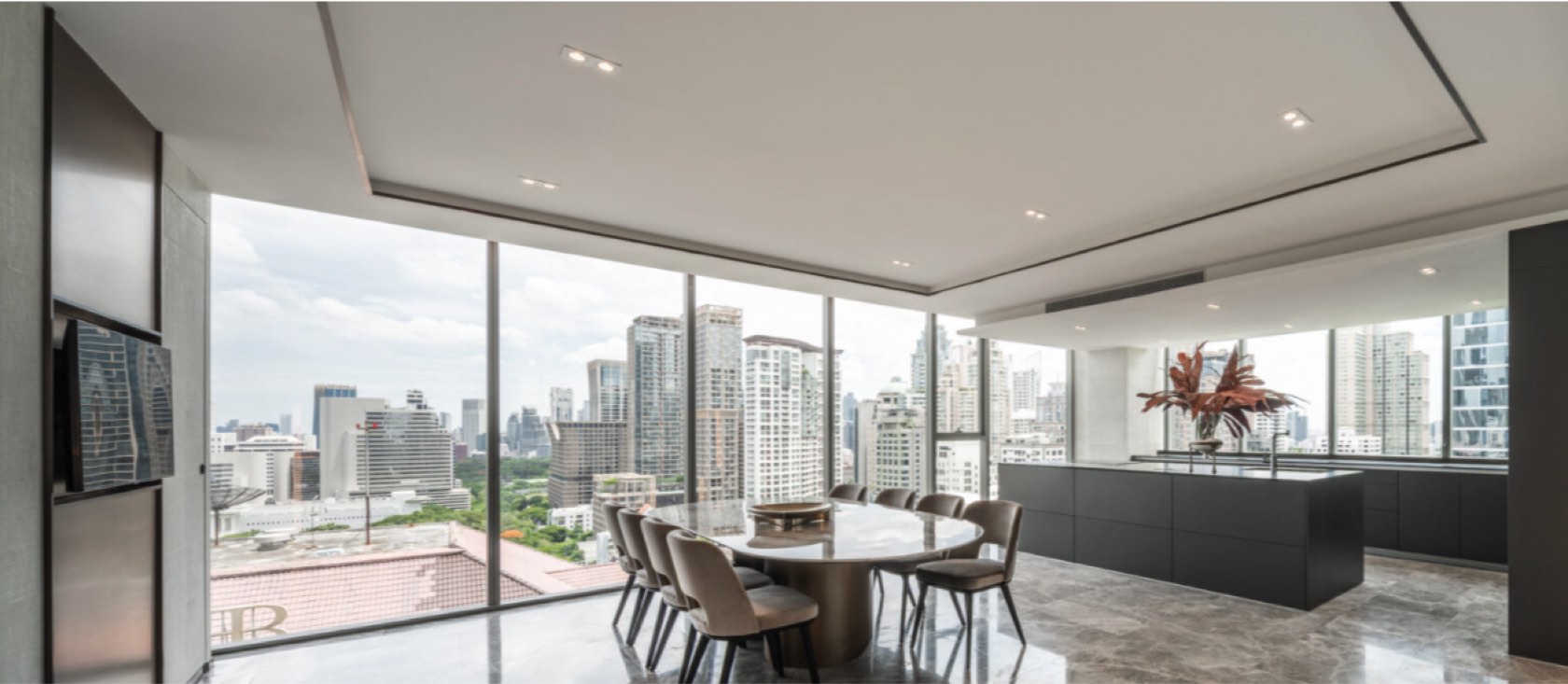 An open dining room and kitchen island with marble floors and skyline views in a Tonson One residence, central Bangkok